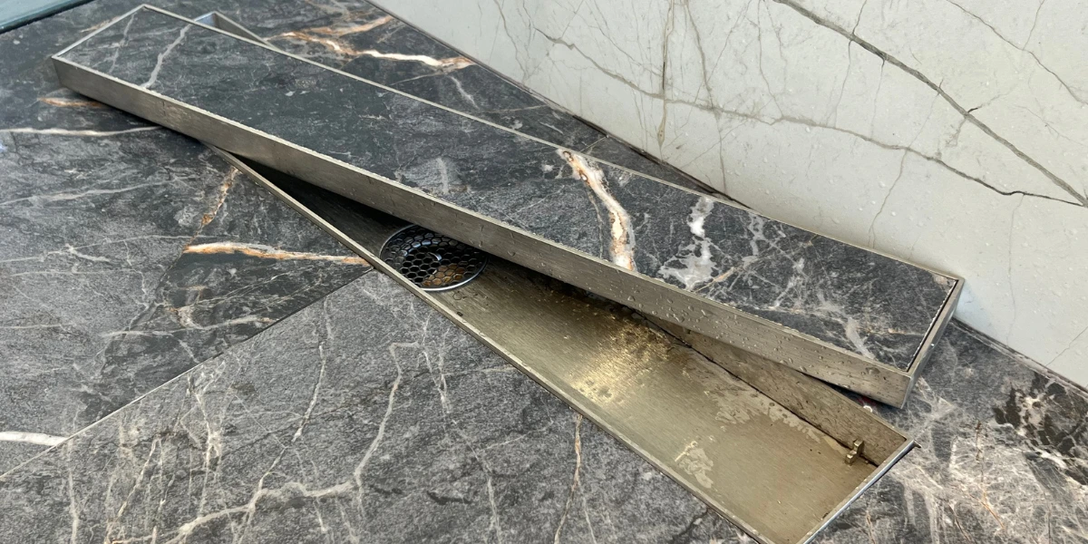 An open tile-insert linear drain showing the internal stainless steel channel and marble cover, demonstrating the versatility of a floor drains manufacturer’s product line.