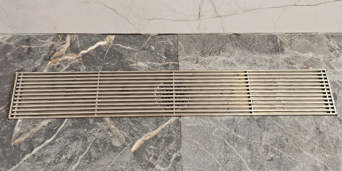 Close-up of a heavy-duty stainless steel linear floor grate on marble tiling, manufactured by a leading floor drains manufacturer for luxury bathrooms.