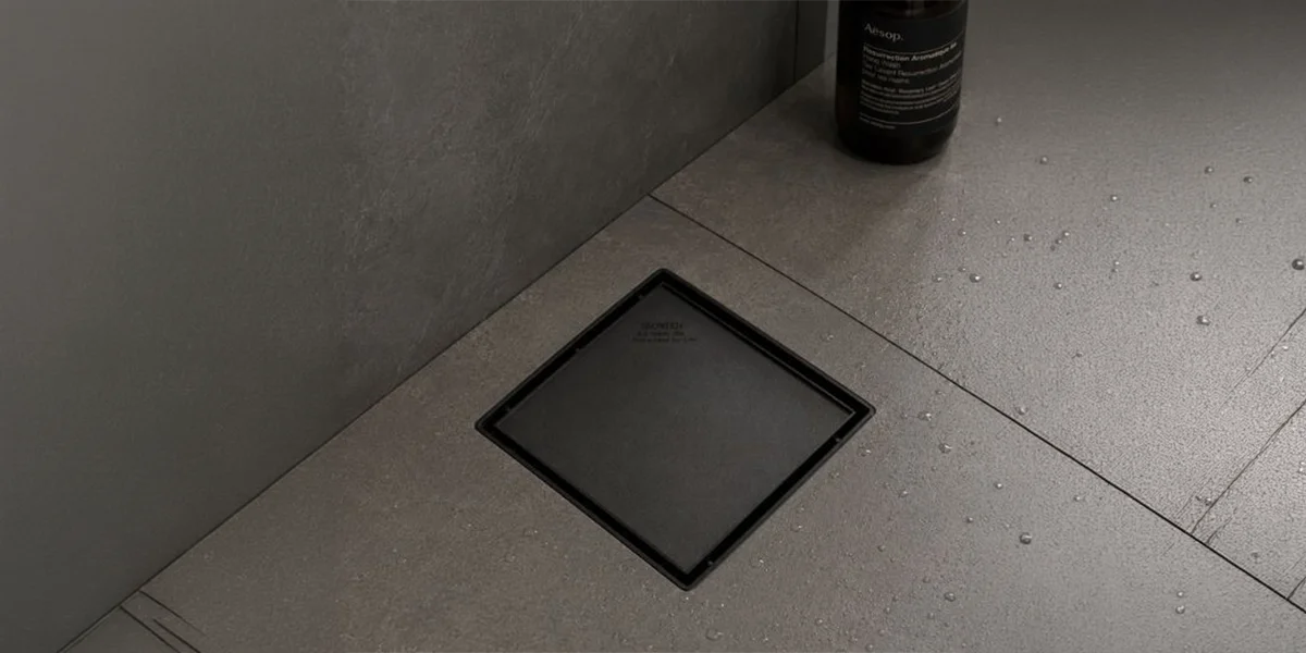 Industrial Floor Drains UAE featuring a sleek black square drain fitted into a tiled bathroom floor.